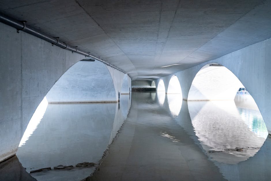 A contemporary concrete tunnel with arched design showcasing water reflections and geometric symmetry.